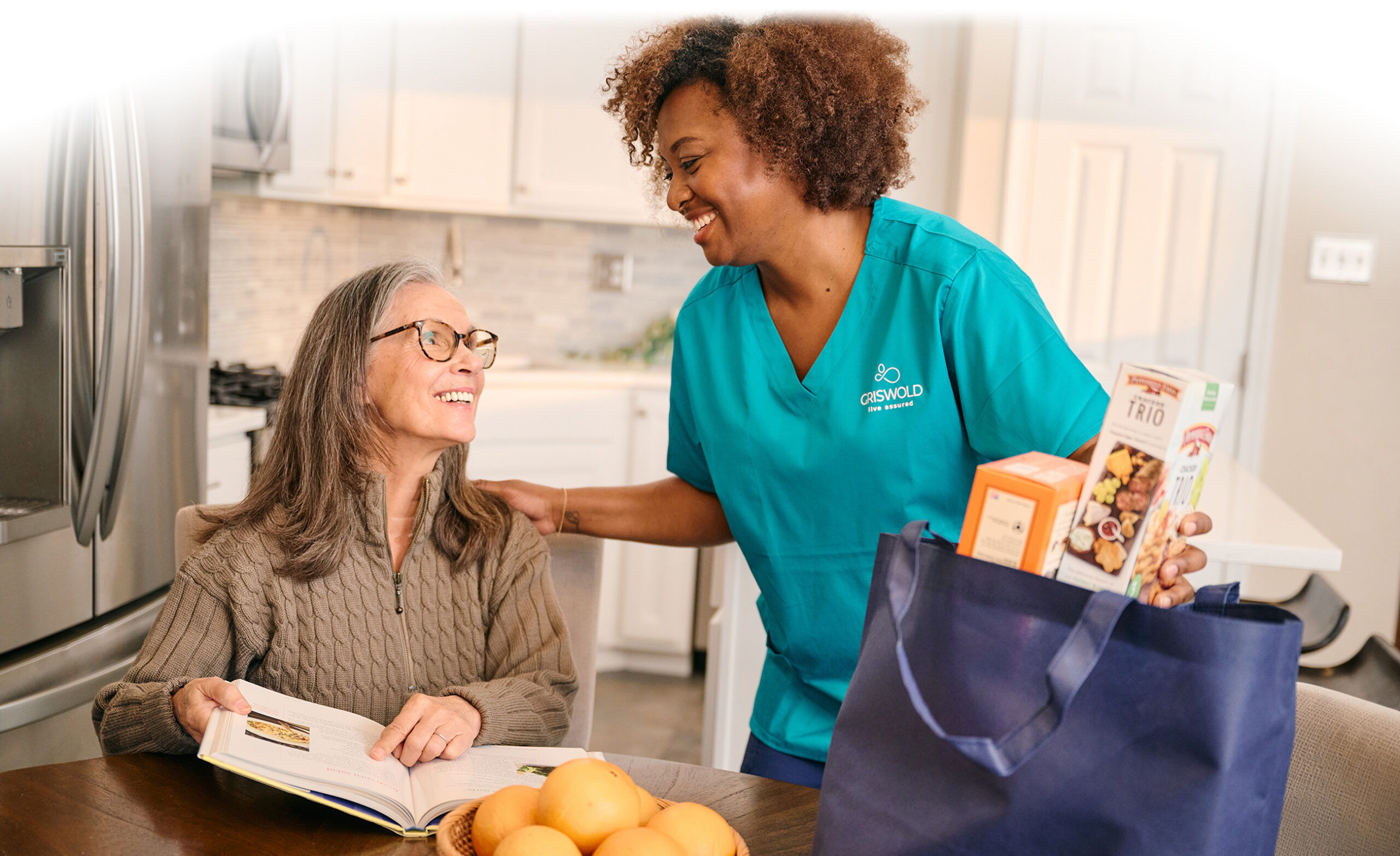 A photo of a Caregiver and client smiling in a kitchen.