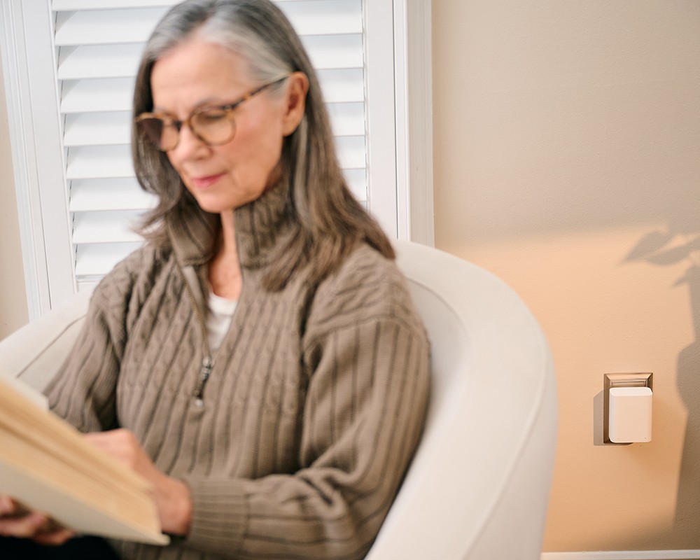 A woman reading with a Sensi pod plugged into the wall behind her.