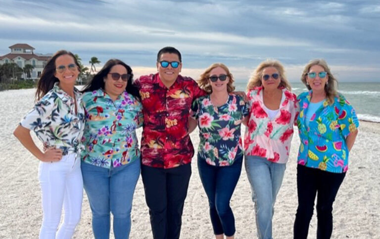 SWFL team wearing bright colored Hawaiian shirts on a sandy beach