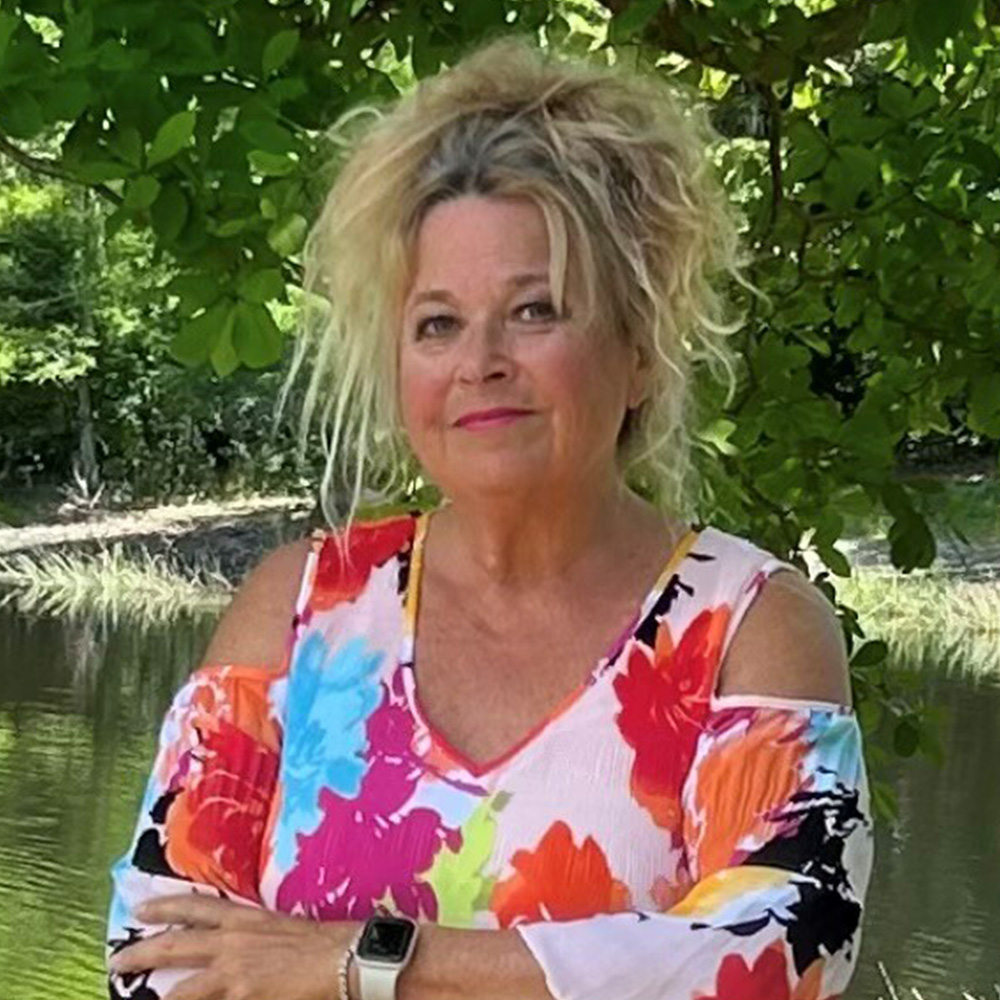 Blonde woman with colorful shirt in front of pond and tree branch