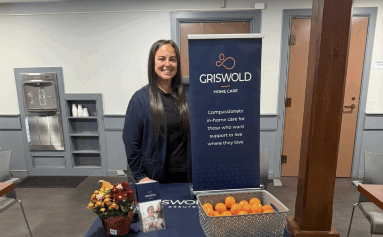 Our Director, Jessica Howard-Ross, tabling at an event. There is a Griswold banner, a basket of oranges, and some flowers on the table.