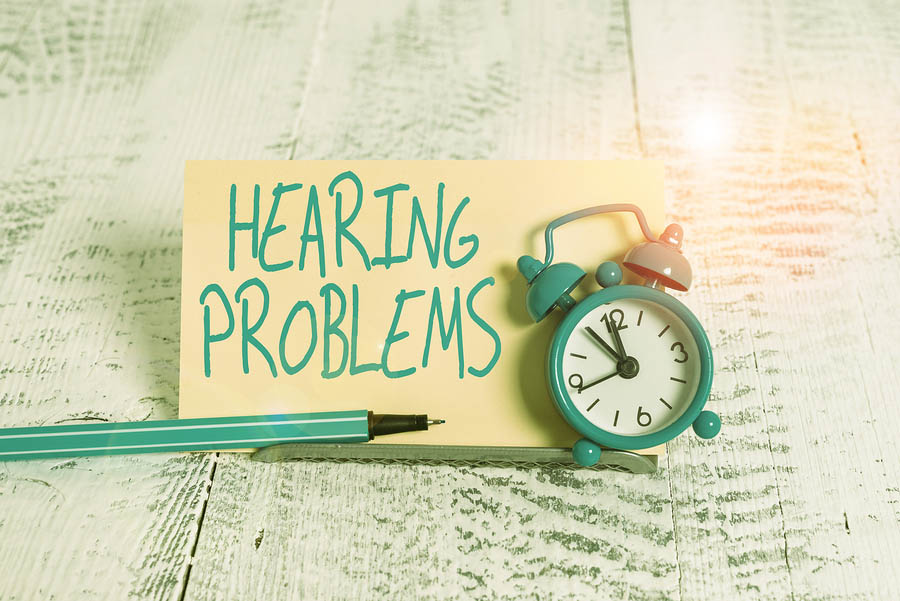 A sign reading "Hearing Problems" sits on a wooden surface next to a pen and a small alarm clock, highlighting the importance of elderly care assistance for those in need.