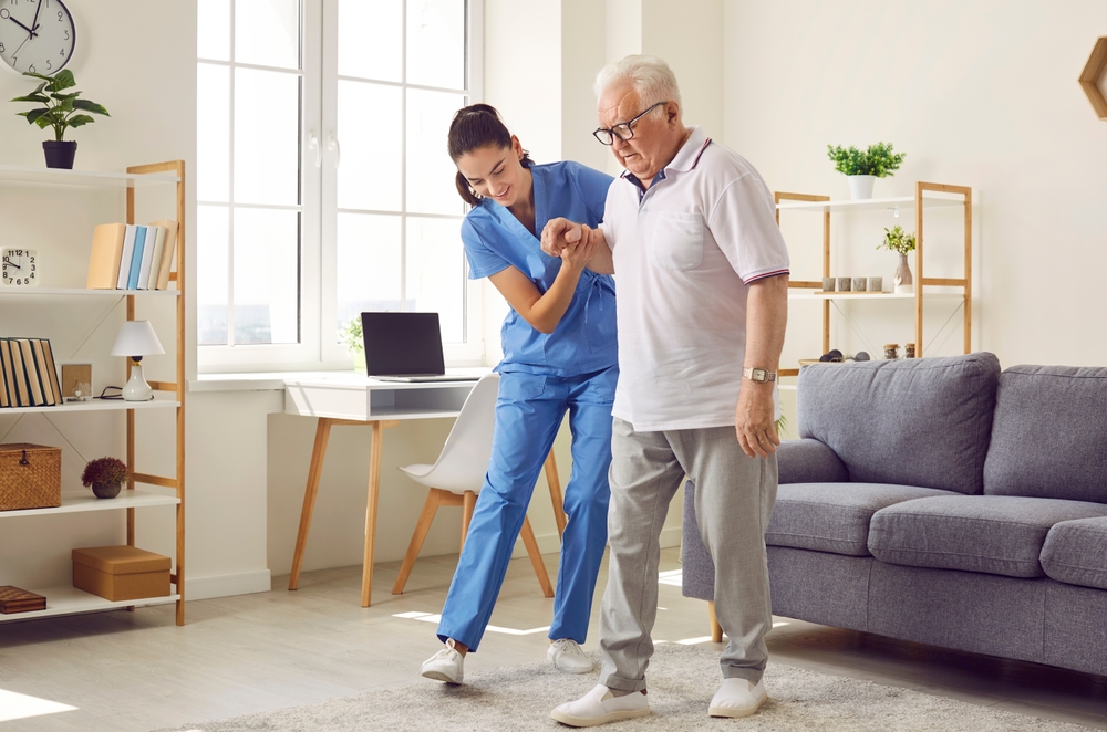 A nurse in blue scrubs assists an elderly man