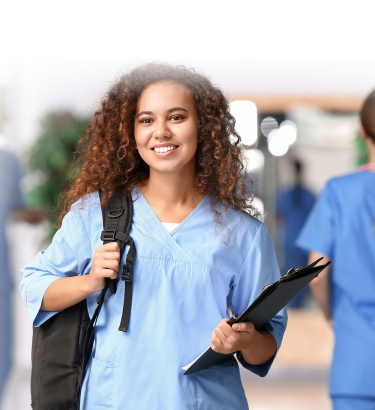 A person in medical scrubs and a backpack smiles while holding a clipboard, representing professional home health care services. Other individuals in similar attire are seen in the background.